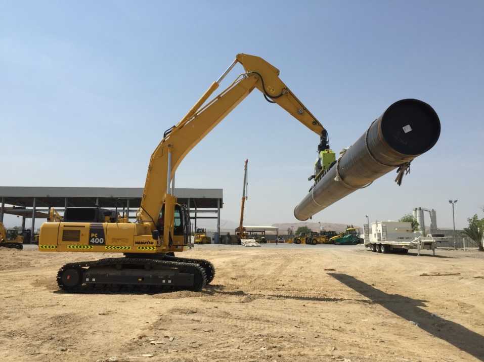 A large yellow komatsu pc 400 excavator performing precision pipe lifting with a vlentec vacuum attachment in an industrial yard.