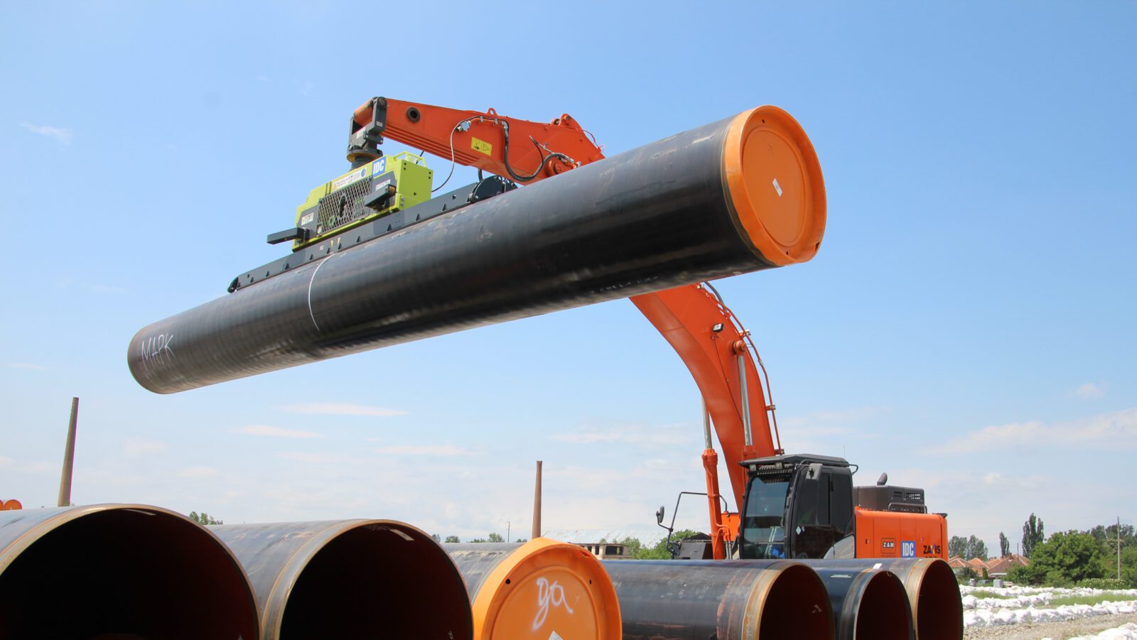 An orange hitachi excavator utilizing a vlentec vacuum lifter for efficient pipe lifting of large diameter coated pipes.